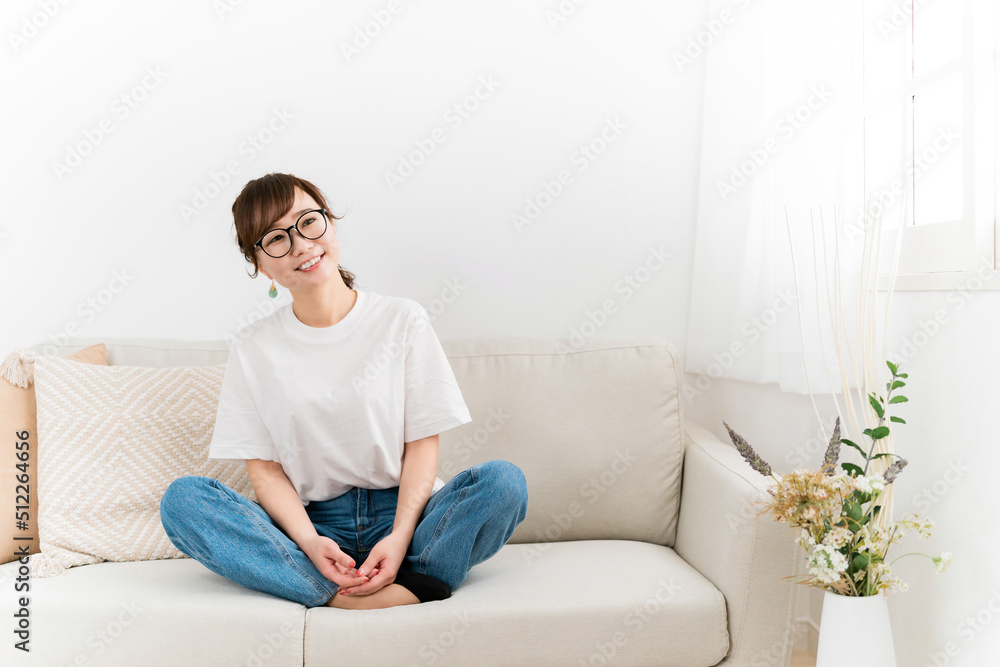 家のソファに座る眼鏡をかけたデニム姿のおしゃれな日本人女性（リラックス）
