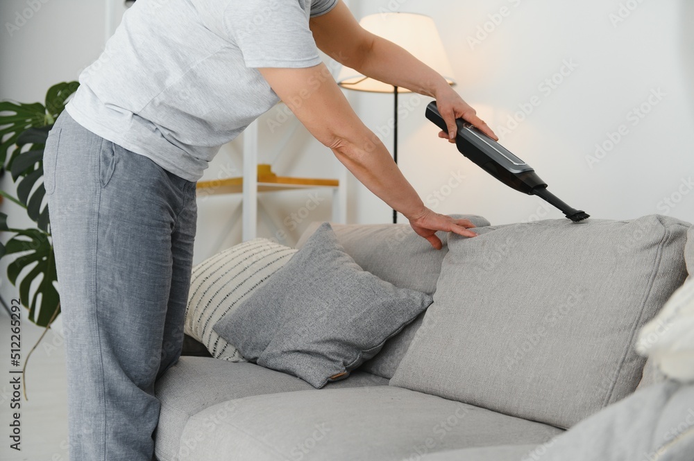 Portrait of senior woman with vacuum cleaner indoors at home, hoovering