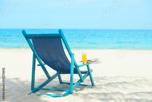Chair with glass of juice and book on sunny beach, tropical beach vacation and travel concept