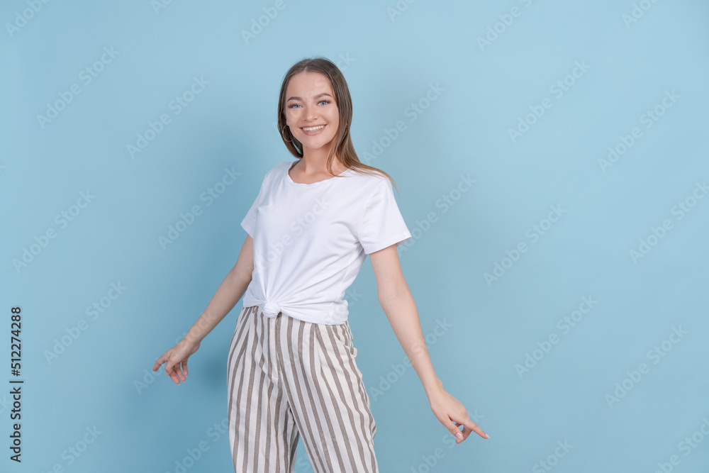 Cute girl dances shyly in studio on blue background in light casual clothes. Beautiful caucasian young woman posing in the studio on a colored background Cute girl dances shyly in studio on blue background in light casual clothes. Beautiful caucasian young woman posing in the studio on a colored background