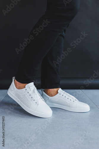 A man in white leather casual sneakers, summer men's sneakers. Man in black jeans