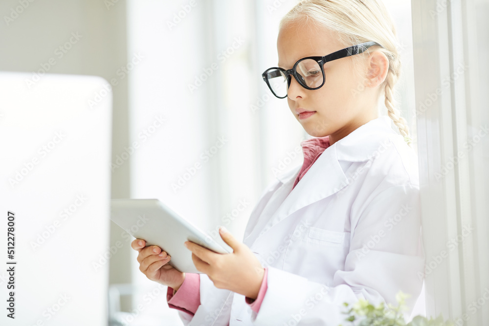 Serious concentrated little girl in big spectacles playing doctor using digital tablet in modern office Serious concentrated little girl in big spectacles playing doctor using digital tablet in modern office