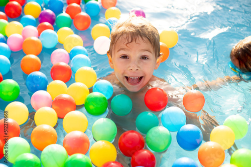 Young child, swimming in the summer in a pool full of colorful balls, enjoying beautiful sunny weather