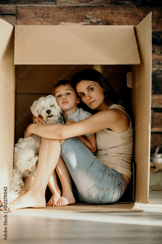 Mother, holding her toddler child in her arms, sitting in cardboard box Mother, holding her toddler child in her arms, sitting in cardboard box