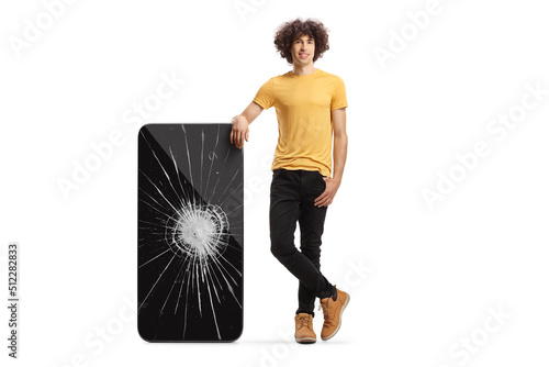 Young man with curly hair stanging next to a smartphone with crushed screen photo