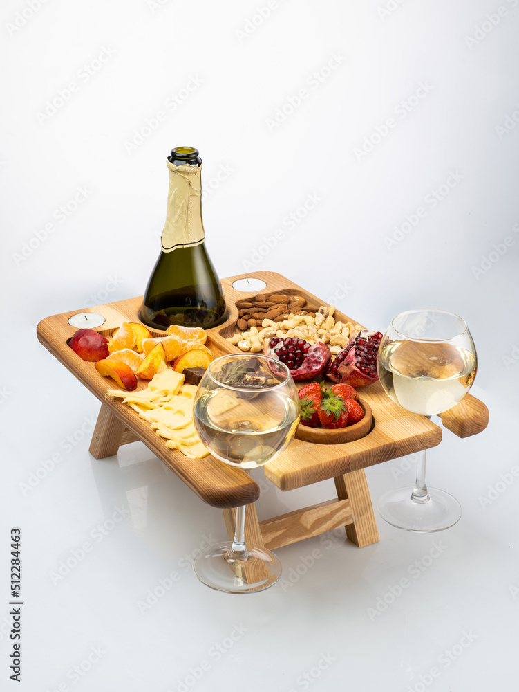 wooden rectangular bowl with legs, a stand filled with fruits, nuts, wine on a white background. Picnic in nature
