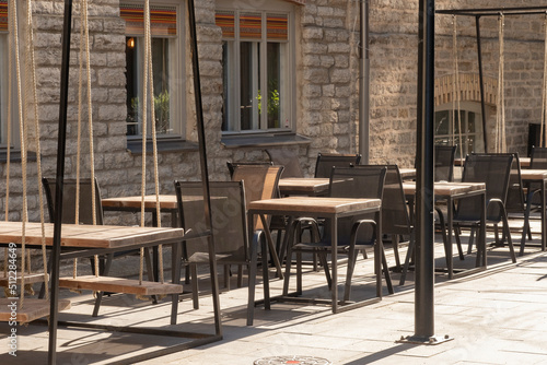 Cafe or restaurant terrace with empty chairs and tables. Summer open air. Eating outside on warm, sunny day. European street view. Hipster style, modern wooden furniture, swing instead of chair © CrunchyBeans