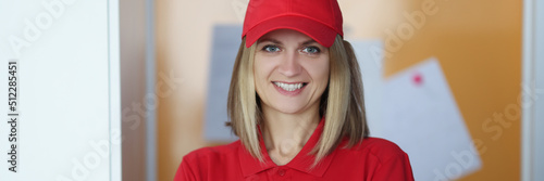 Happy blonde lady courier in red shirt and cap uniform
