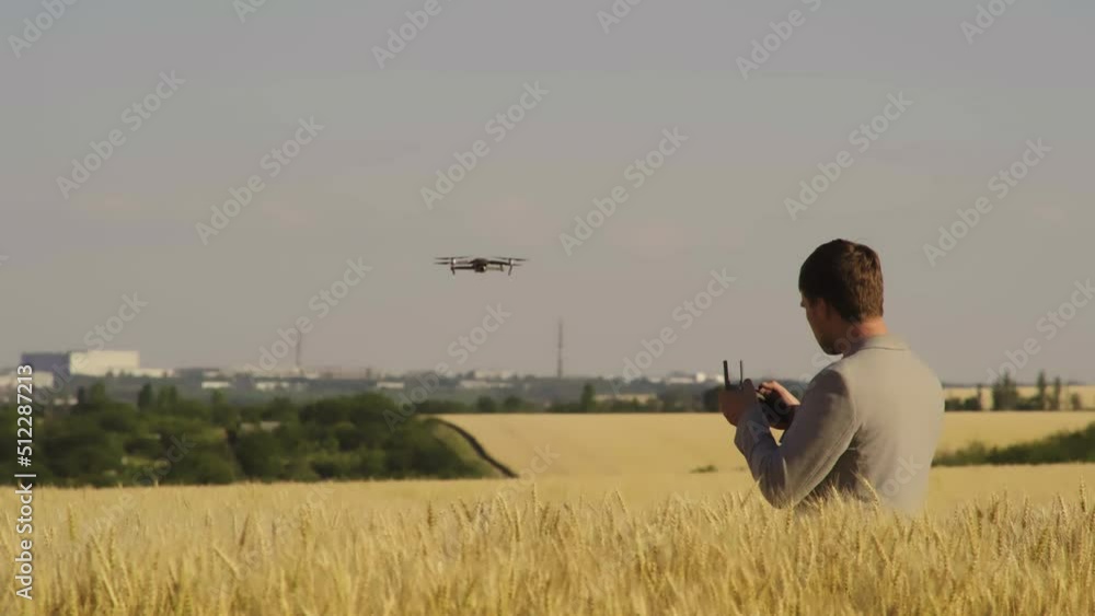 A close-up of a Ukrainian male farmer standing in a golden wheat field controlling a drone flying over the field. The farmer is using a tablet device as a controller. Technology in agriculture. A close-up of a Ukrainian male farmer standing in a golden wheat field controlling a drone flying over the field. The farmer is using a tablet device as a controller. Technology in agriculture.
