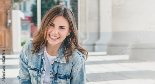 student girl sits on the background of the university and smiling. Cute young woman laughing looking at the camera, web banner. copy space