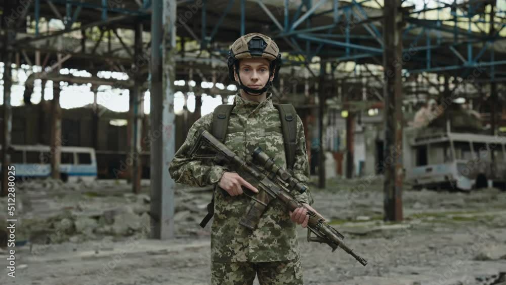 Trained military female standing with automatic rifle in her hands and looking at camera. Portrait of middle aged woman in uniform posing on old ruined plant after combat training. Trained military female standing with automatic rifle in her hands and looking at camera. Portrait of middle aged woman in uniform posing on old ruined plant after combat training.