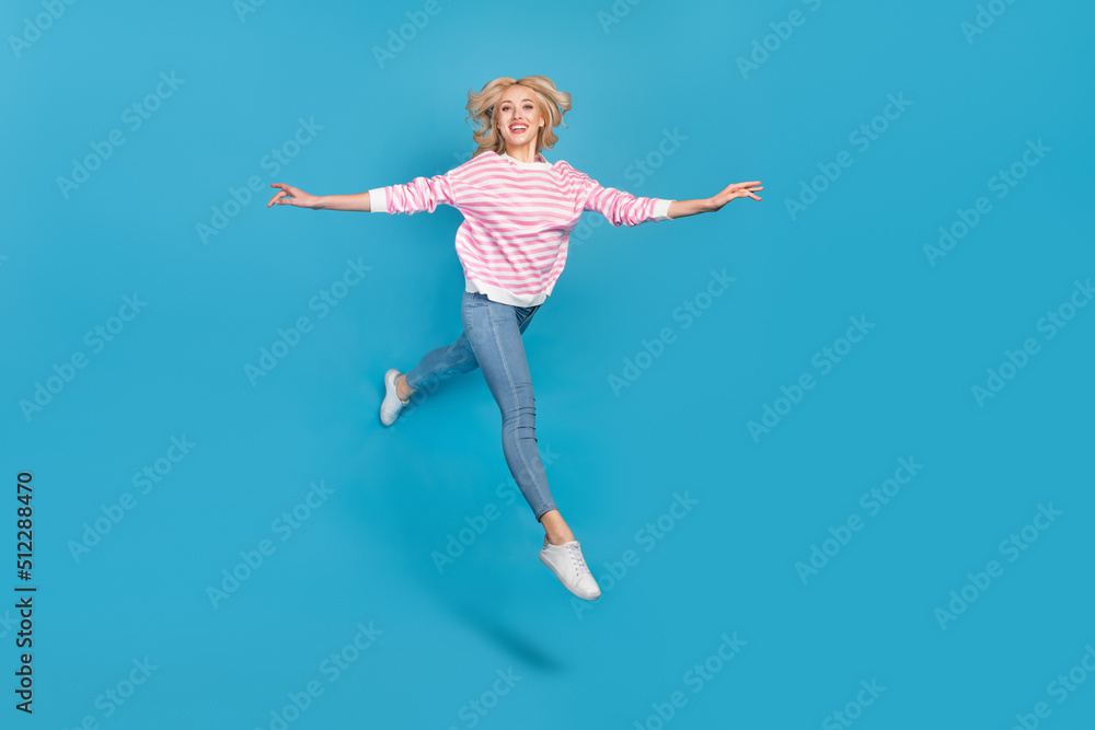 Photo of adorable pretty woman wear striped sweater jumping high running arms sides isolated blue color background