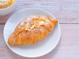 Croissant with cream and almonds on white circle plate and coffee cup over wooden table. Close up, space for text..