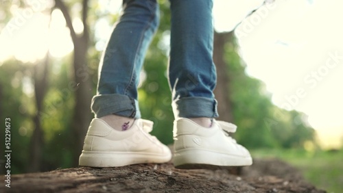 baby girl playing in the forest park. close-up child feet walking on a fallen tree log. happy family kid dream concept. a lifestyle child in sneakers walks on a fallen tree in park