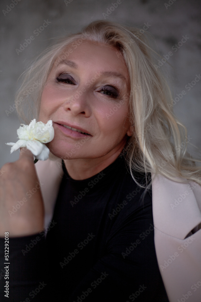 Portrait of a beautiful woman aged 60, against a gray wall. Senior dressed black thin polo-necked sweater and jacket