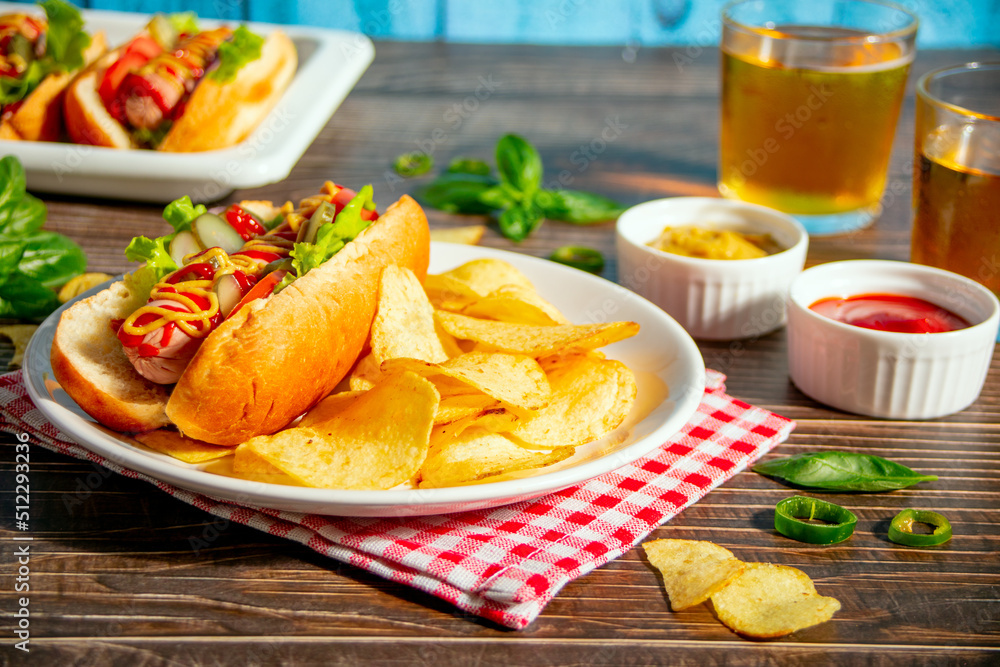 Delicious homemade hotdogs with chips and glasses of beer on wooden table. Delicious homemade hotdogs with chips and glasses of beer on wooden table.