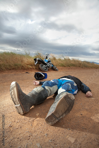 A motorcyclist lying on a dirt road after what seems like an accident.