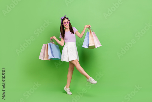 Full body photo of cool brunette lady hold bags wear glasses t-shirt skirt shoes isolated on green background