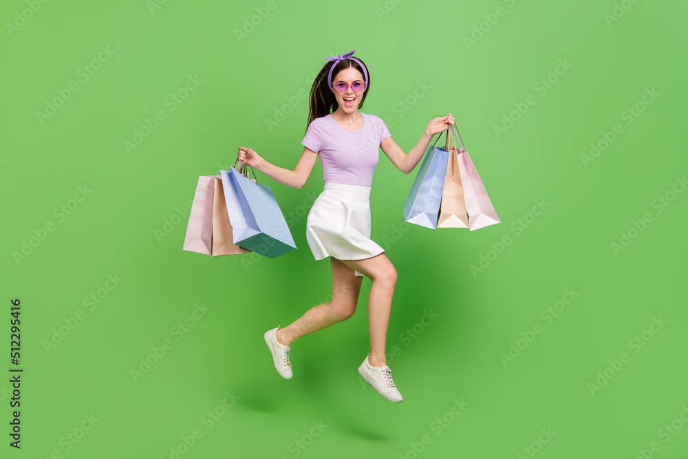 Full body photo of impressed brunette lady hold bags run wear glasses t-shirt skirt sneakers isolated on green background Full body photo of impressed brunette lady hold bags run wear glasses t-shirt skirt sneakers isolated on green background