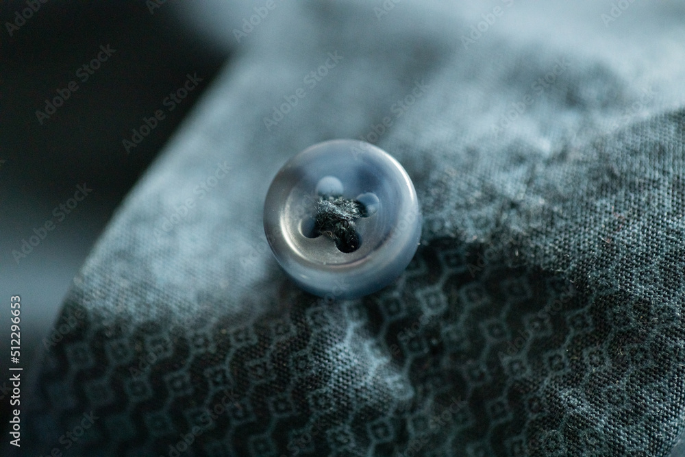 A button on a shirt close-up, a fragment of a turquoise-blue shirt, a wavy pattern on the fabric A button on a shirt close-up, a fragment of a turquoise-blue shirt, a wavy pattern on the fabric