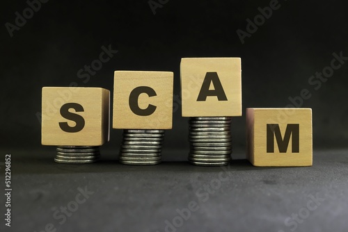 Investment scam, fraud and Ponzi scheme concept. Stack of coins on wooden blocks with word scam in dark black background. photo