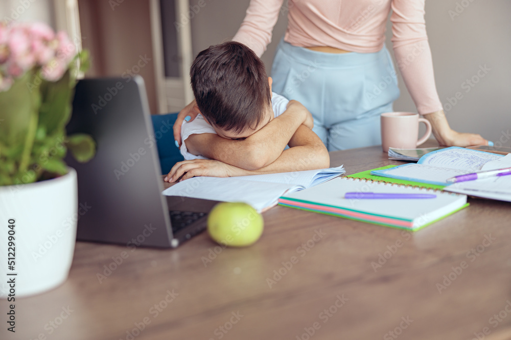 Little lazy schoolboy putting his head on hands on table, crying or sleeping at mother. Little lazy schoolboy putting his head on hands on table, crying or sleeping at mother.