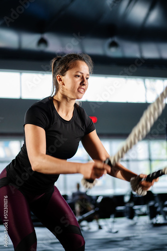 Powerful woman training battle ropes at cardio workout in dark gym. Professional athlete exercise fitness sport club equipment. Strong bodybuilder lifting weights. Athletic person effort © Guys Who Shoot
