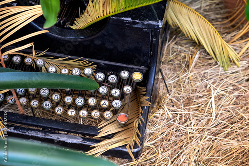 abandoned vintage black typewriter with black peeling paint close-up with the Russian alphabet on a haystack in green vegetation