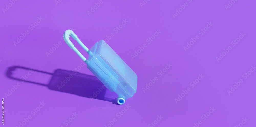 Toy blue suitcase on purple background with a hard shadow. Banner with copy space Toy blue suitcase on purple background with a hard shadow. Banner with copy space