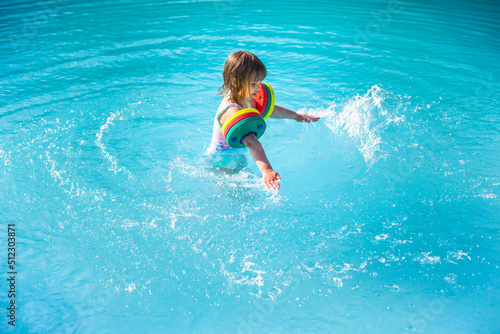 Kind mit Schwimmflügel planscht im hellblauen Pool. Child with water wings splashes in the light blue pool.