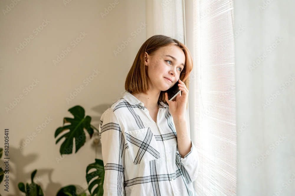 Beautiful businesswoman using phone at home office. Cozy office workplace, remote work, e-learning concept. Young happy smiling femail talking on mobile cellphone arranging meeting, share information