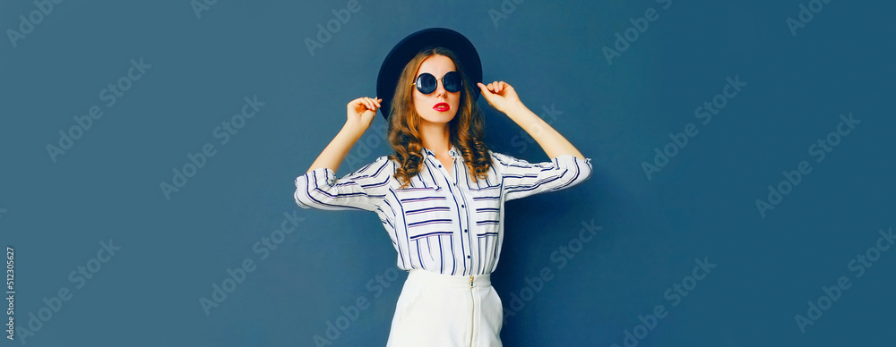 Portrait of beautiful young woman wearing white striped shirt, black round hat on dark blue background - obrazy, fototapety, plakaty 