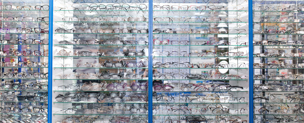 Sunglasses on optics shelves. Large selection of glasses for vision correction. The glasses are laid out on the store's glass shelves in neon lighting.
