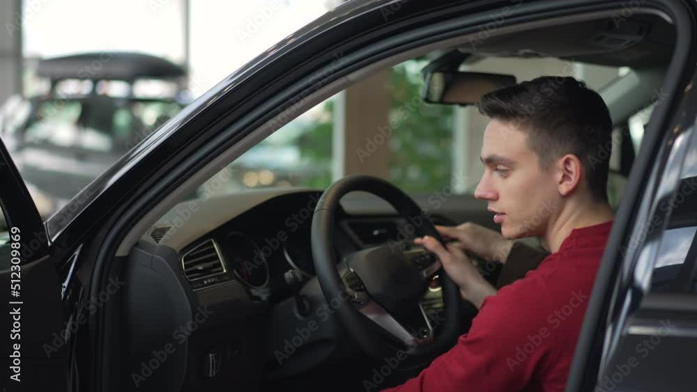 Young son, old father are sitting in new car and talking while shopping in company spbd. 4k Close view of caucasian guy sits in transport and holds steering wheel, talks to his dad and looks with Young son, old father are sitting in new car and talking while shopping in company spbd. 4k Close view of caucasian guy sits in transport and holds steering wheel, talks to his dad and looks with