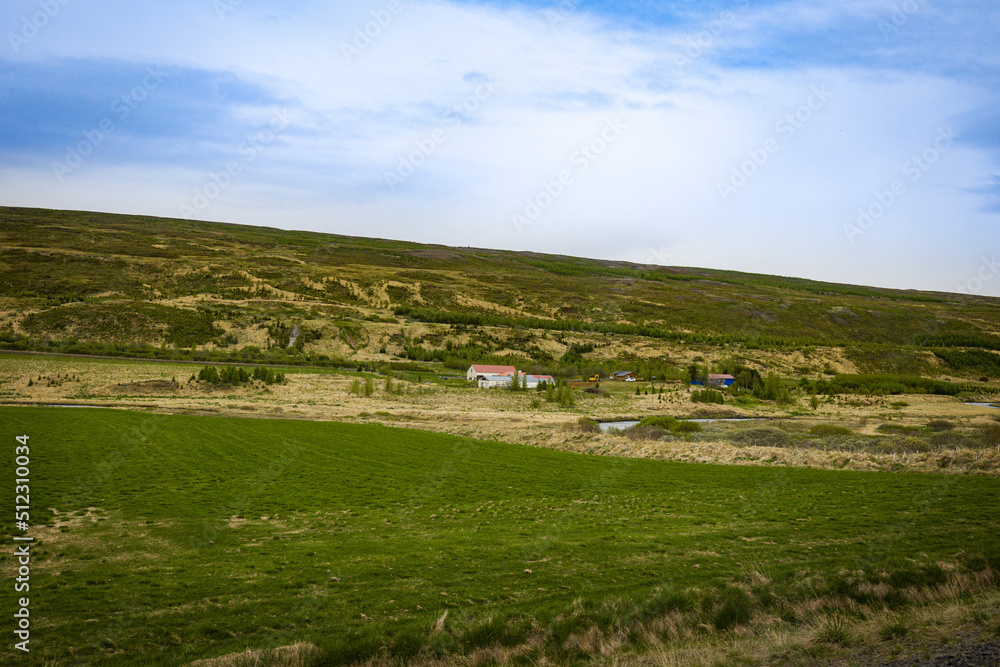 Hills and meadows in the rural Icelandic community. Small farm building in the distance.