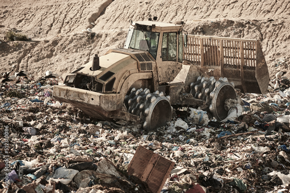 Fototapeta premium Heavy machinery shredding garbage in an open air landfill. Pollution