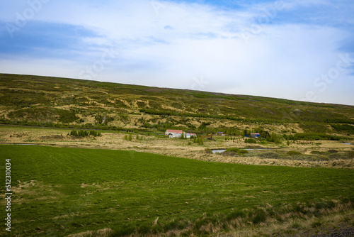 Hills and meadows in the rural Icelandic community. Small farm building in the distance.