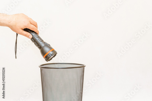 The flashlight is thrown into the trash,can for disposal and recycling.White,gray background,selective focus,copy space.