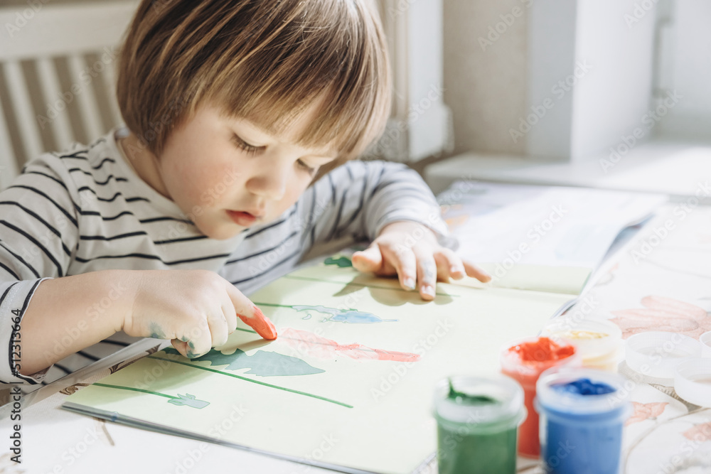 Finger painting. Portrait of cute little boy painting with fingers at home. Close-up of child's hand in colorful paints. Early education concept. Sensory play. Development of fine motor skills. Finger painting. Portrait of cute little boy painting with fingers at home. Close-up of child's hand in colorful paints. Early education concept. Sensory play. Development of fine motor skills.