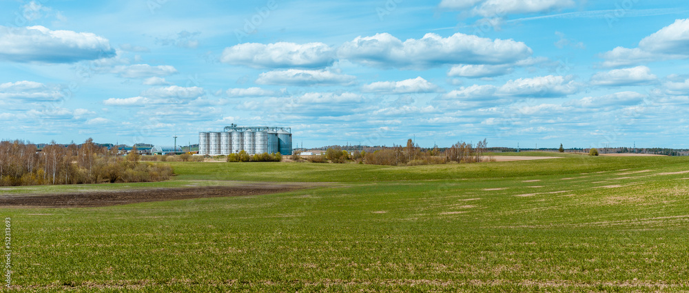 Silver silos on agro manufacturing plant for processing drying cleaning and storage of agricultural products, flour, cereals and grain.Beautiful summer blue sky,clouds,green meadow landscape.Banner. Silver silos on agro manufacturing plant for processing drying cleaning and storage of agricultural products, flour, cereals and grain.Beautiful summer blue sky,clouds,green meadow landscape.Banner.