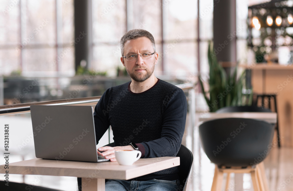 Successful adult man with glasses works on a laptop in a cafe Successful adult man with glasses works on a laptop in a cafe