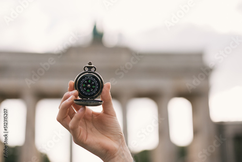 Old classic navigation compass in hand on Brandenburg Gate background, symbol of tourism 