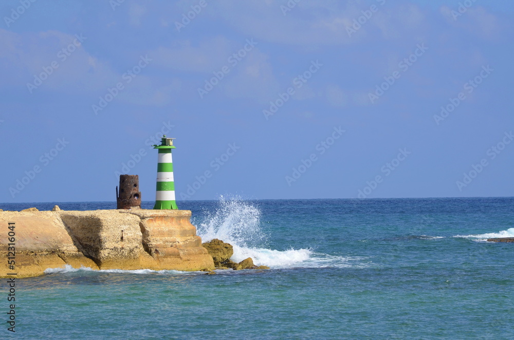 Mediterranean Sea. Port of Jaffa in Israel. Green lighthouse, waves crashing against the stone. Concept: travel, sea holidays, yachting, sailing. Place for text