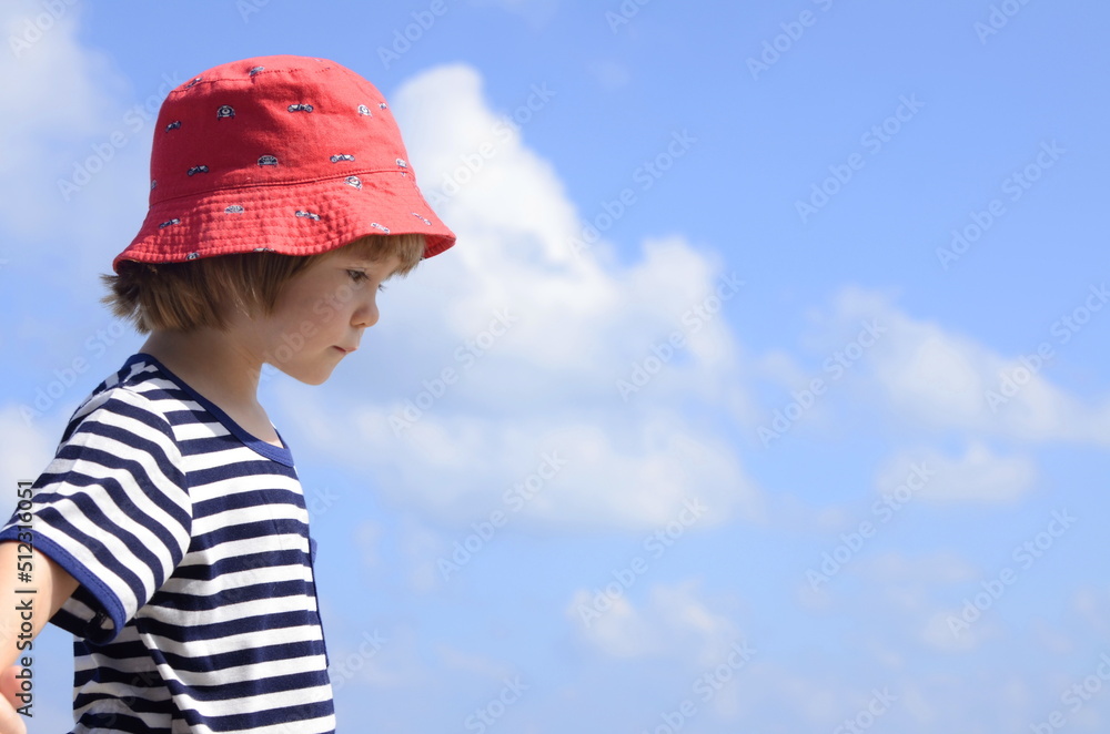 A cute little boy in a vest and a red panama hat against a beautiful sky. Portrait of a child. Travel preparation, family vacation, trip with children. Space for text