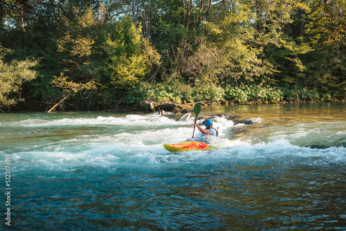 Caucasian man kayaking over the mountain river rapids, with the beautiful rocky bank and green forest in the background. Water sport