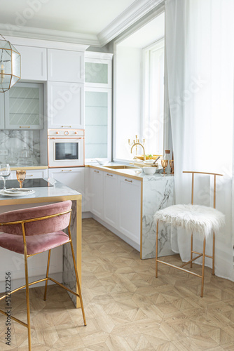 a close view of the white stylish kitchen with a cooking island in the luxurious interior of a modern apartment in light colors with stylish furniture.