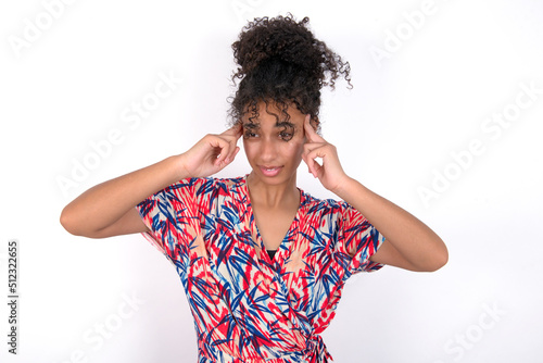 Young African American woman wearing colourful dress over white wall concentrating hard on an idea with a serious look  thinking with both index fingers pointing to forehead.