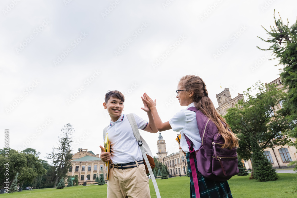 Obraz premium Smiling interracial schoolkids giving high five in park.