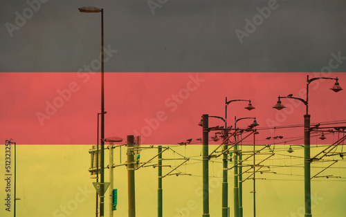 Germany flag with tram connecting on electric line with blue sky as background, electric railway train and power supply lines, cables connections and metal pole overhead catenary wire