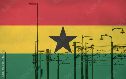 Ghana flag with tram connecting on electric line with blue sky as background, electric railway train and power supply lines, cables connections and metal pole overhead catenary wire
